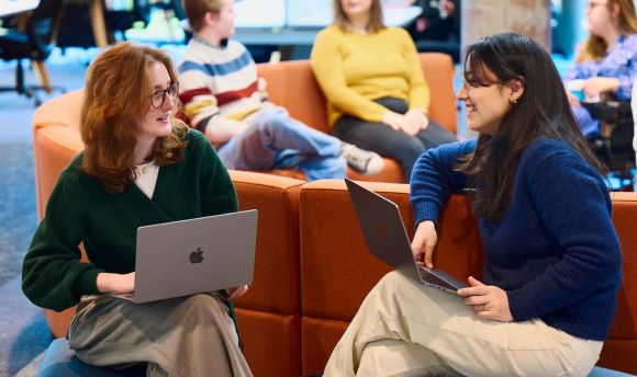 Two young female student smiling and chatting while working on a laptop