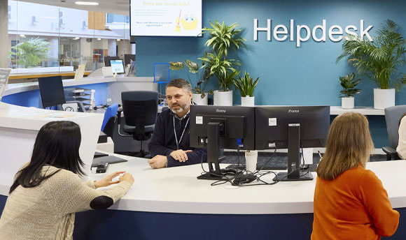 A male member of staff at the Helpdesk speaks with a female student.