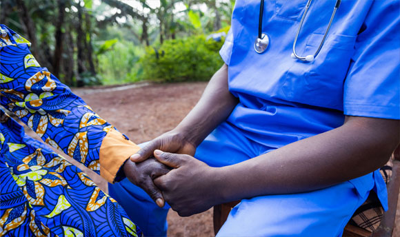 A close up of a health worker holding the hand of a patient, they are both wearing bright blue coloured clothing.