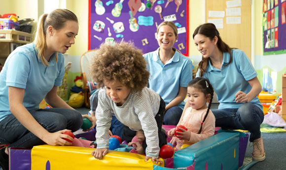 Three nursery staff playing games with two small children.