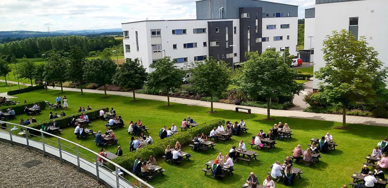Dozens of students sitting on outdoor seating in their graduation robes.