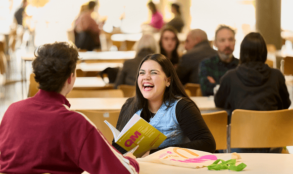 Male and female student laughing in the canteen holding a QMU prospectus. 