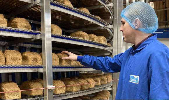 A man wearing food-safe clothing inspecting loaves of bread
