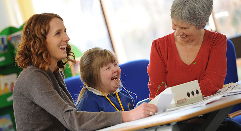A young girl with Downs Syndrome using speech and language therapy equipment with two adults
